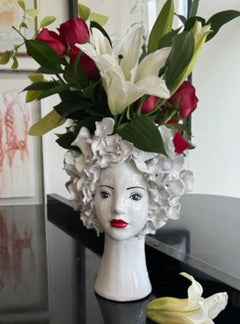 White ceramic head-shaped vase with red and white flowers on a black table.