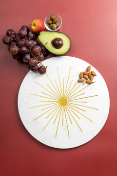 Elegant marble tray with gold sunburst design, fruits, and nuts.